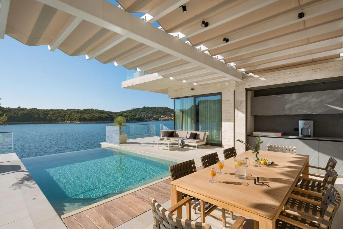 Infinity pool and outdoor dining table under a pergola with sea views at Villa Anthon