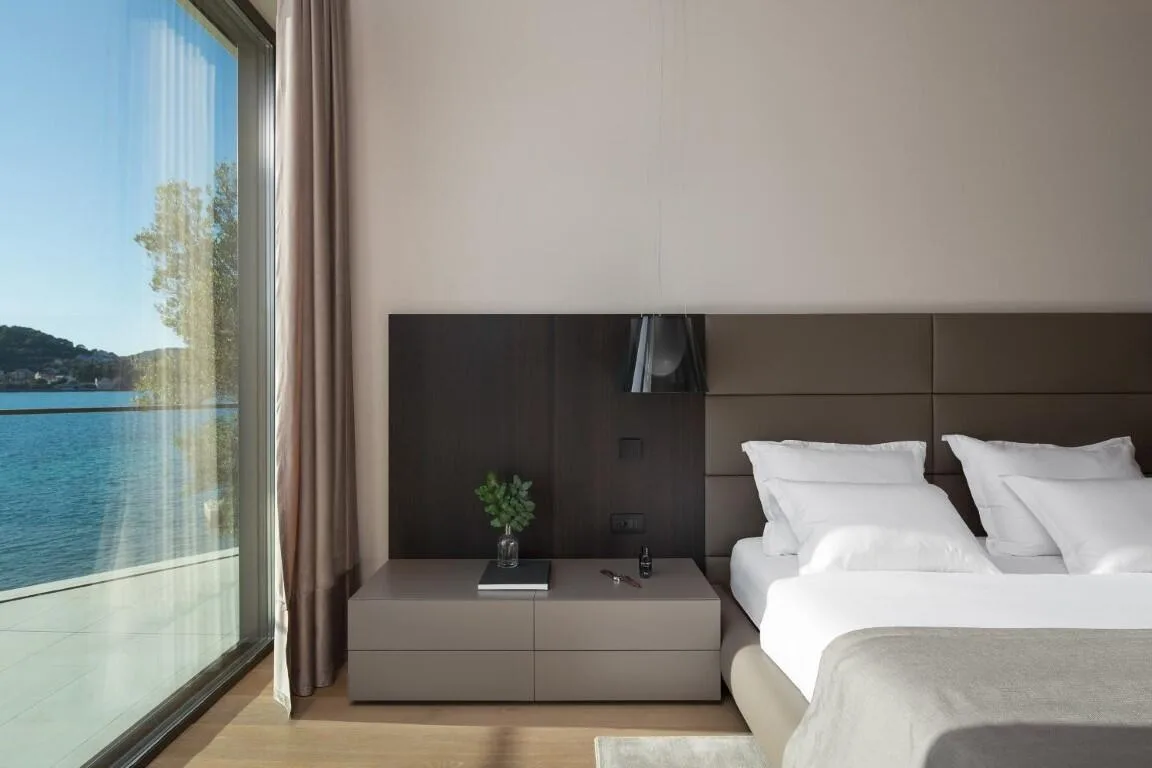 King-size bed beside a full-height window with sea view at Villa Anthon