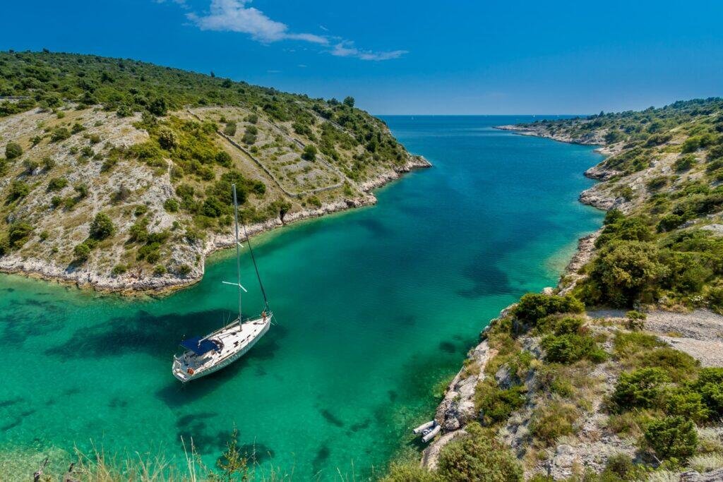 Sailing boat anchored in a turquoise bay along the rocky, pine-covered Adriatic coast near Dubrovnik
