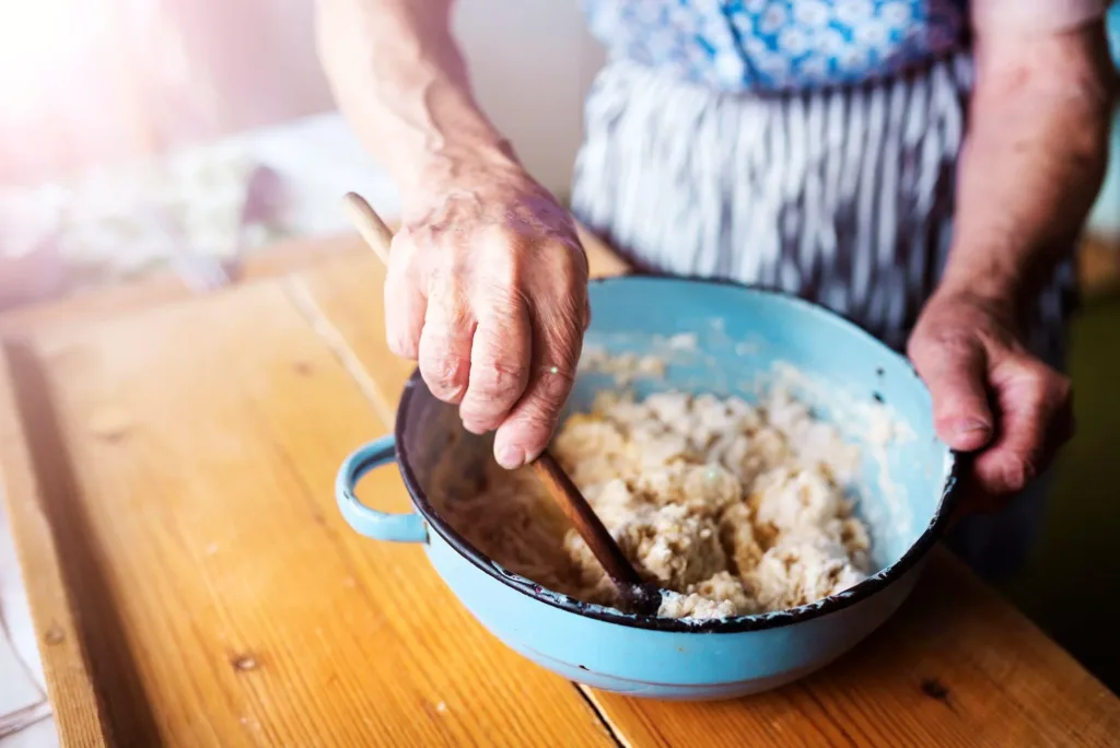 Hands stirring traditional dough in a blue enamel bowl with a wooden spoon during a private cooking class in Dubrovnik