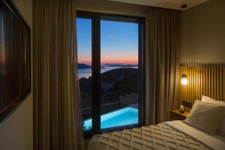 Schlafzimmer mit Blick auf den beleuchteten Pool und das Meer bei Sonnenuntergang in der Villa Ó