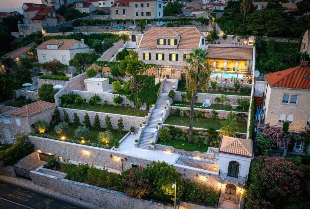 Luftaufnahme des historischen Anwesens Villa La Rose und seiner Gärten, die bei Einbruch der Dunkelheit in Pile, Dubrovnik, beleuchtet sind