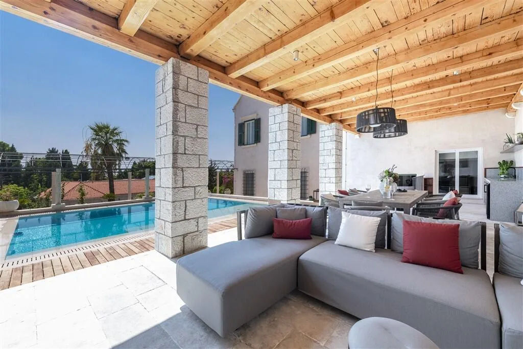 Covered outdoor lounge with grey sofas beside the pool at Villa La Rose