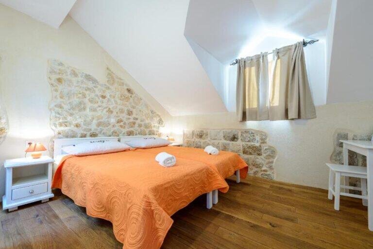 Twin bedroom with orange bedspreads and stone wall at Villa Zeus