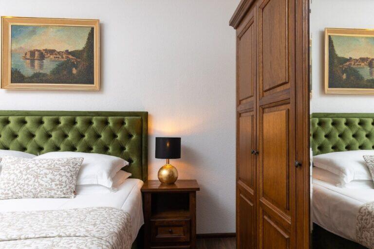 Schlafzimmer mit grüner Samtkopfteil und antiker Garderobe in Villa Le Jardin
