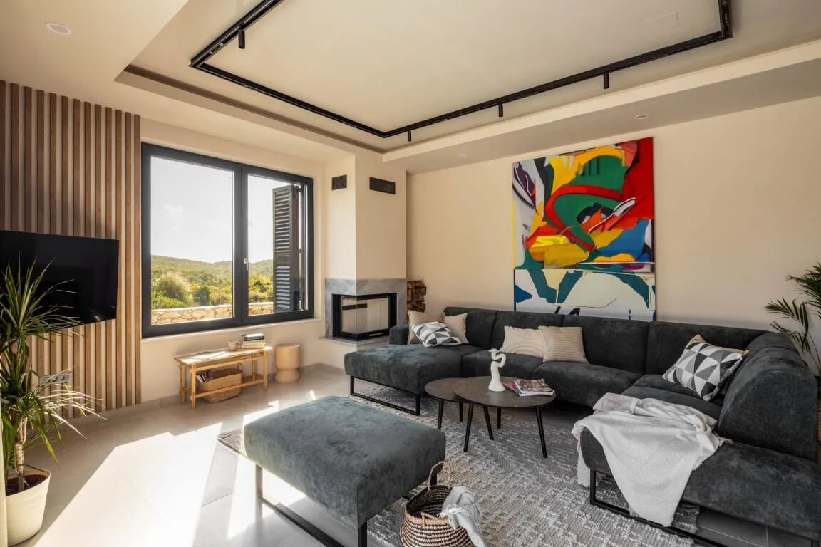 Living area with grey sofa, artwork and countryside window view at Villa Petra