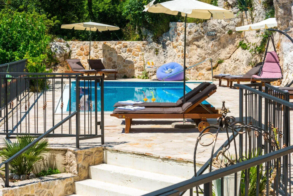 Heated pool with sun loungers and parasols beside rocky cliffs at Villa Zeus, Mlini