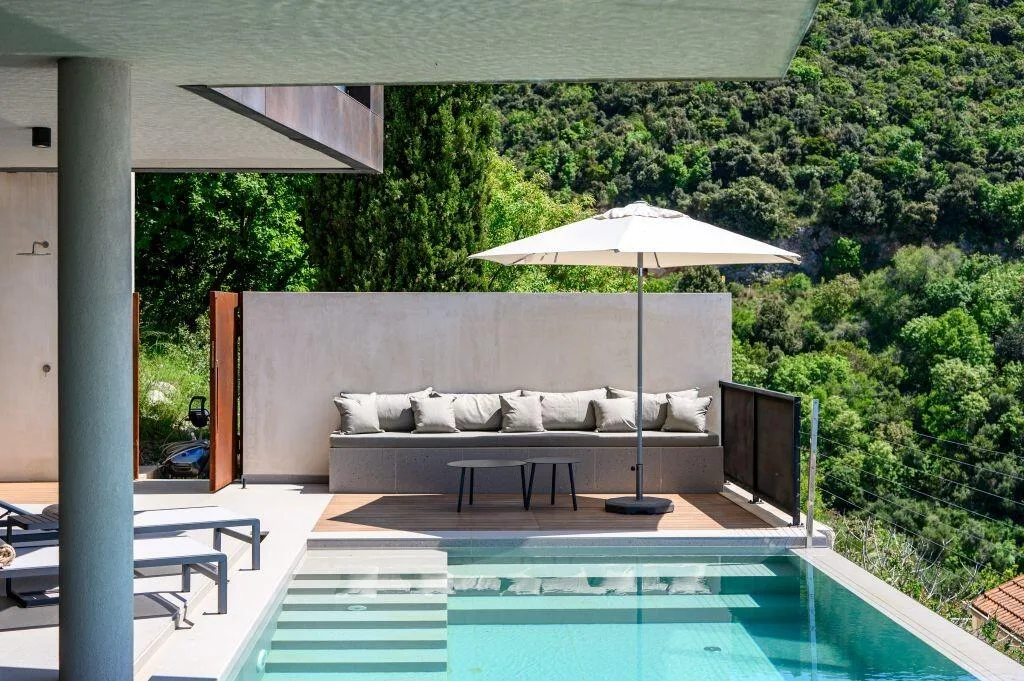 Pool with built-in lounge and parasol surrounded by greenery at Villa Atreeum