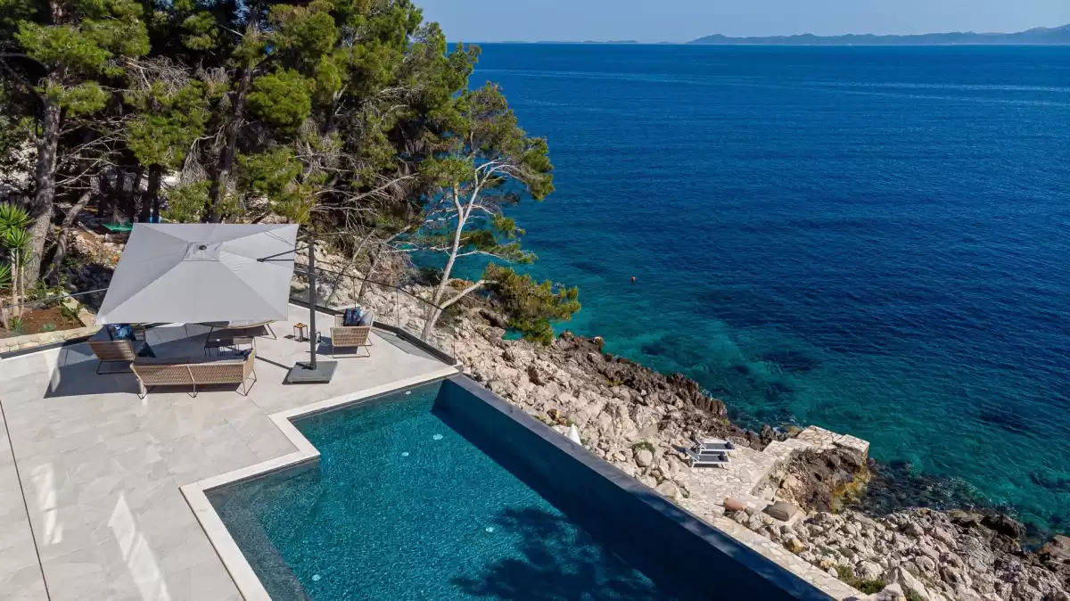 Infinity pool and lounge terrace above the rocky coastline at Villa Sansarea