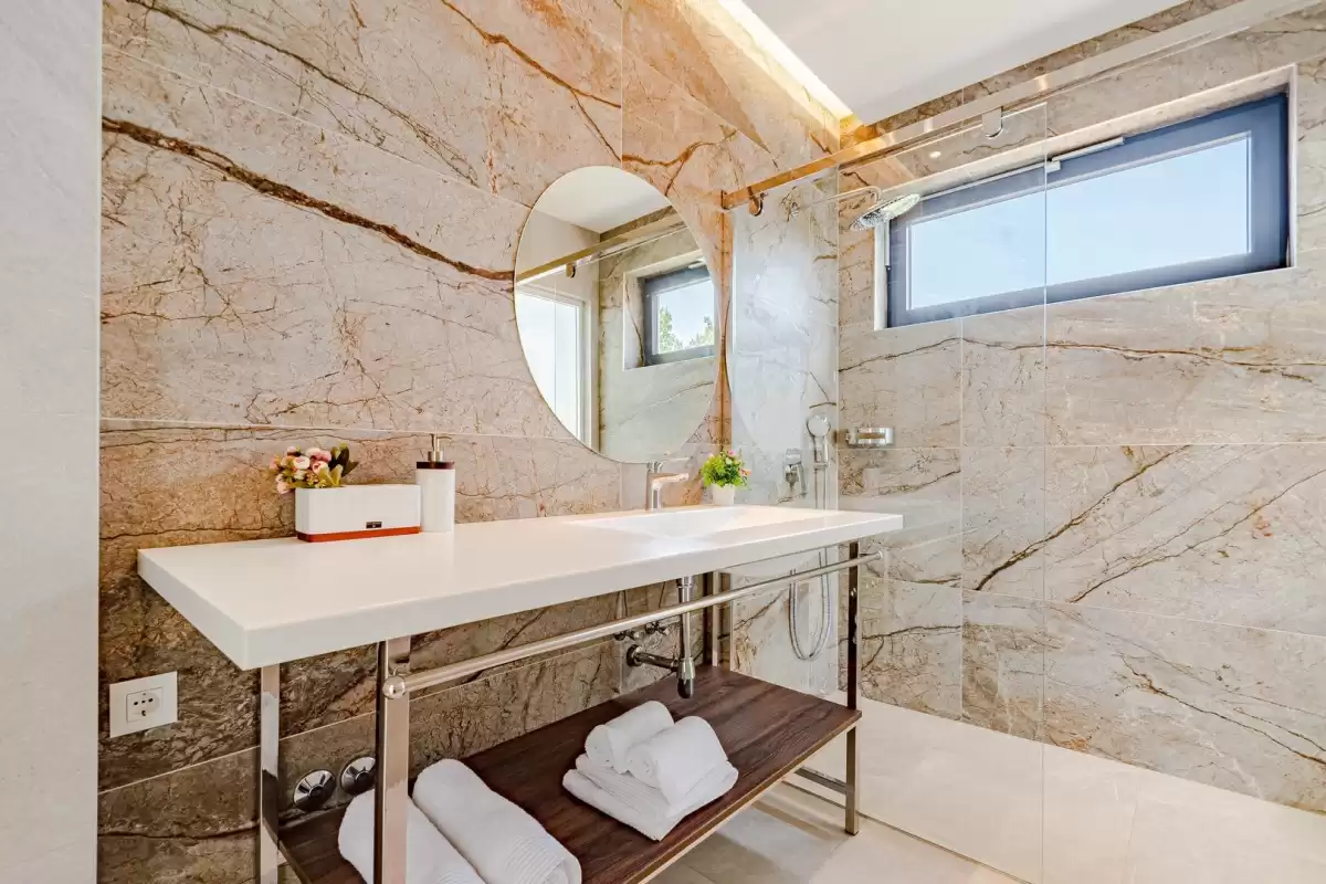 Marble bathroom with round mirror and washbasin at Villa Sansarea