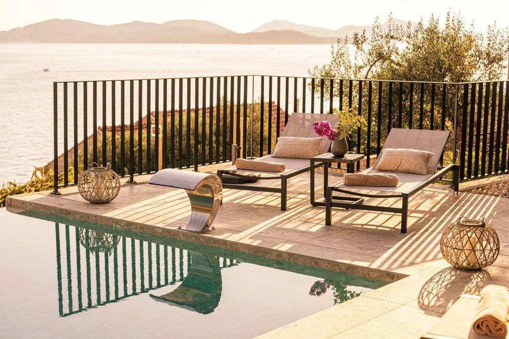 Plage en bois avec des chaises longues au-dessus de la piscine à débordement à Villa Eleven au coucher du soleil