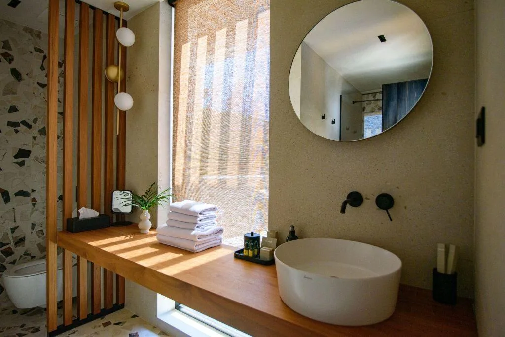 Salle de bains avec lavabo en forme de vase, miroir rond et vanité en bois à Villa Eleven