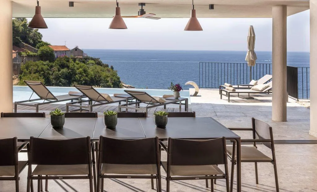 Table de repas extérieure pour dix personnes sous une terrasse couverte avec vue sur la piscine et la mer à Villa Eleven
