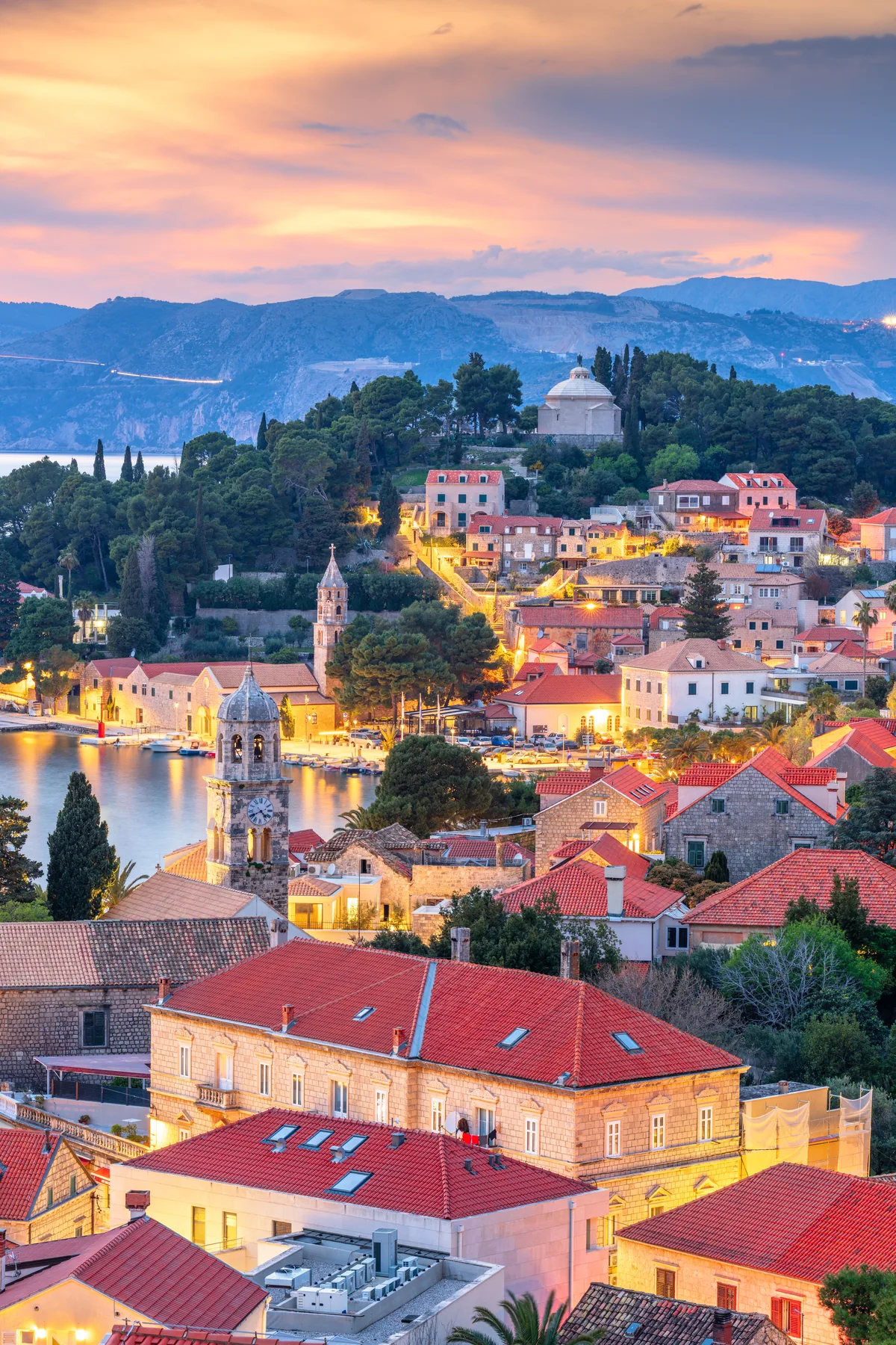 Cavtat old town at dusk with the clock tower, harbour lights and the Račić Mausoleum above the red rooftops