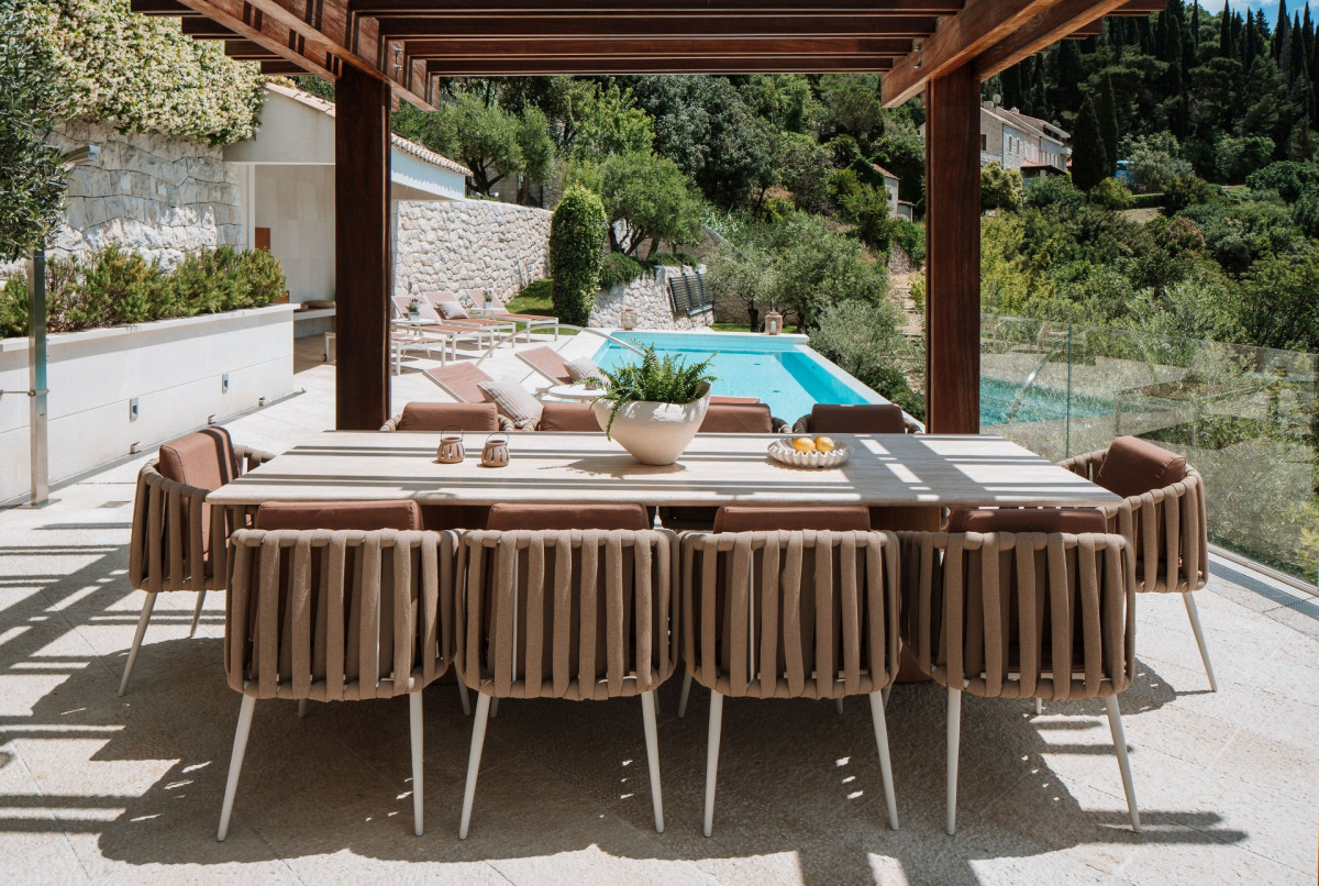 Großer Außenküchentisch mit Wickerstühlen unter einer Holzpergola neben dem Pool in der Villa Blazia