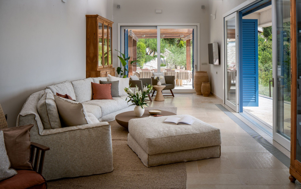 Helles Wohnzimmer in der Villa Blazia mit einer cremefarbenen Sofa, einem Ottomane und Glasfenstern, die auf die Terrasse hinausgehen