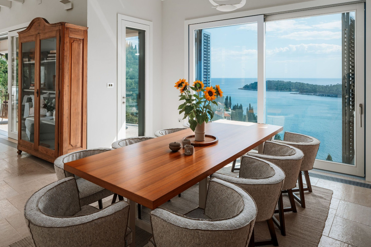 Esszimmer in der Villa Blazia mit einem Holzschreibtisch, sechs Stühlen und einem großen Fenster mit Blick auf das Meer und eine Insel
