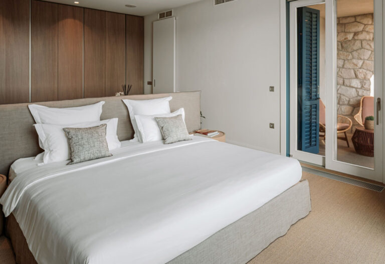 Schlafzimmer in der Villa Blazia mit einem großen Bett, einer Holztreppe an der Decke und einer Glaswand zur Terrasse