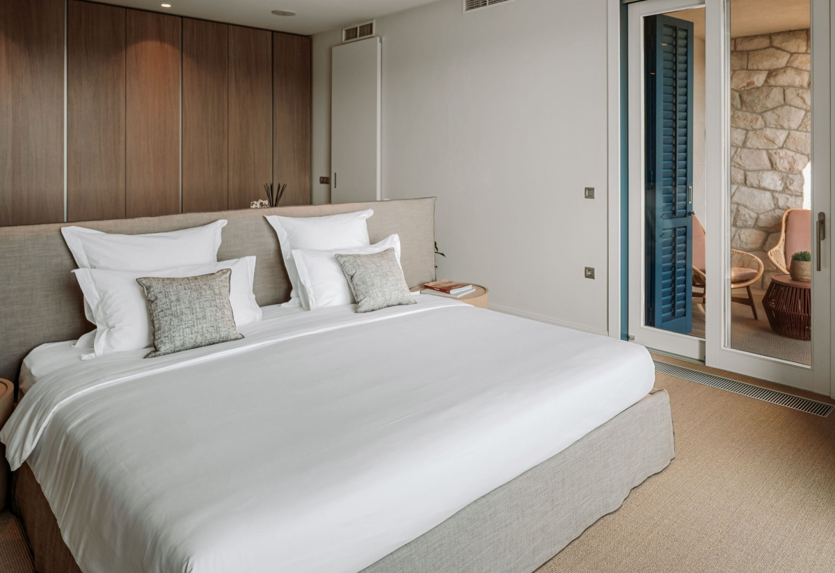 Schlafzimmer in der Villa Blazia mit einem großen Bett, einer Holztreppe an der Decke und einer Glaswand zur Terrasse