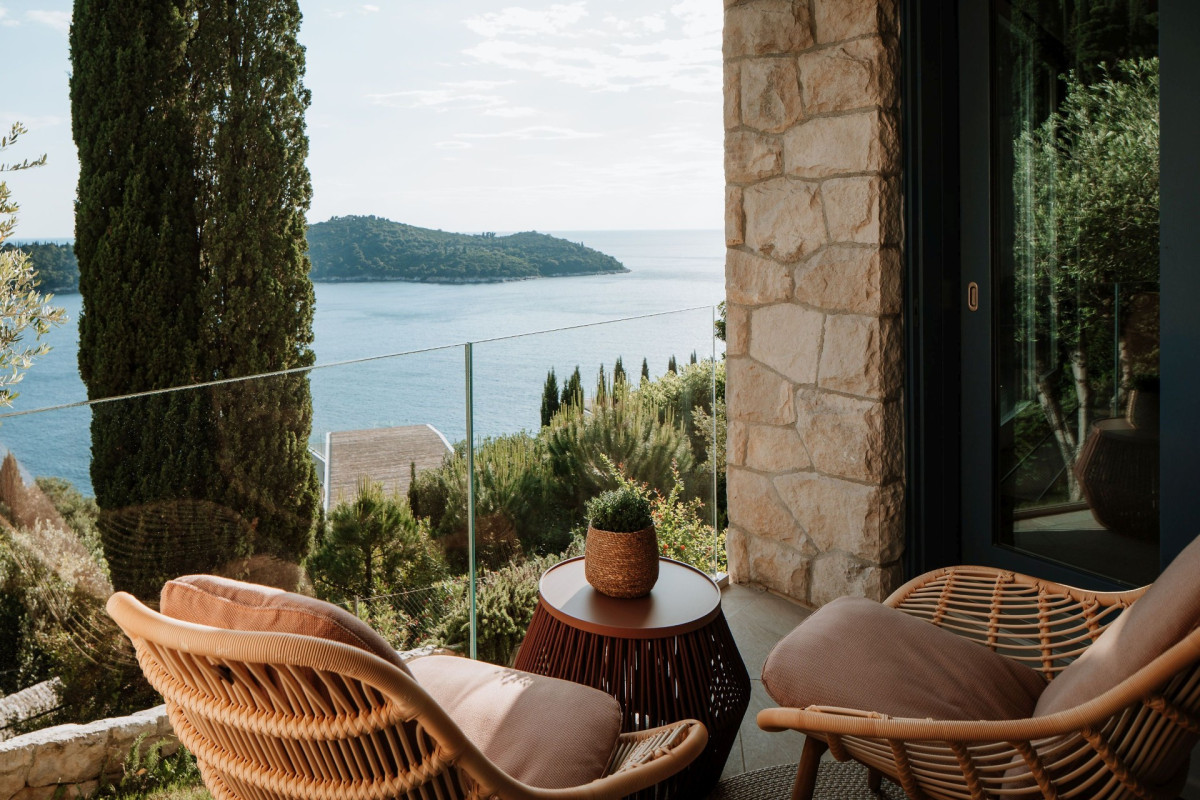 Balkon mit Gestellstühlen aus Weiden und Glasgeländer in der Villa Blazia mit Blick auf das Meer und die Insel