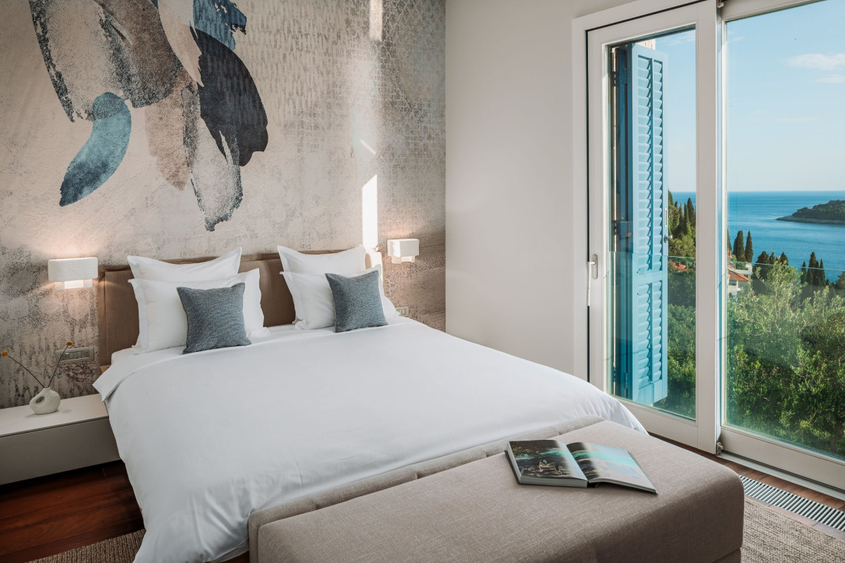 Schlafzimmer in der Villa Blazia mit einem großen Bett, einer künstlerischen Wandmalerei und Fenstern mit Meerblick