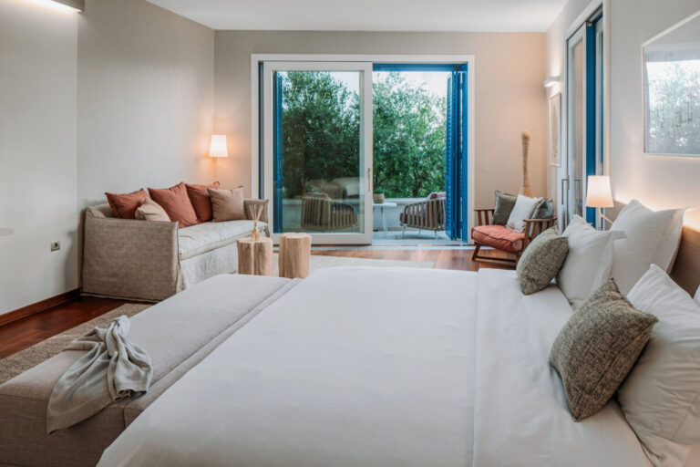Schlafzimmer in der Villa Blazia mit einem Doppelbett, einem Sitzbereich mit Sofa und Glasfenstern zur Gartenpartie