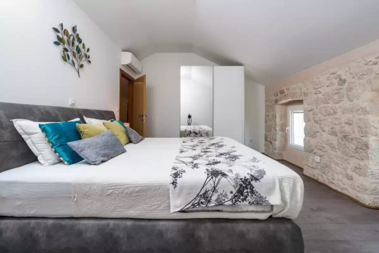 Schlafzimmer mit Doppelbett, abfallender Decke und freiliegender Steinwand im House Brenum, Čelopeci