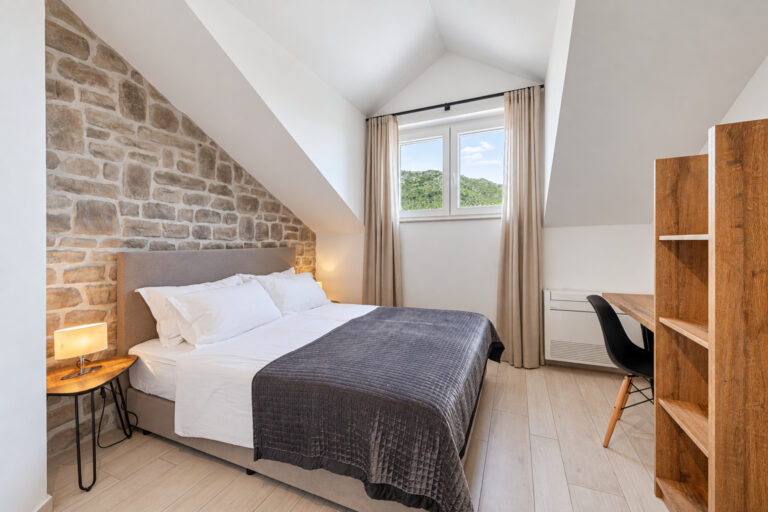 Schlafzimmer mit Kingsize-Bett, Steinmauer und Fenster mit Blick auf die grüne Hügellandschaft im Noah House in Zaton bei Dubrovnik