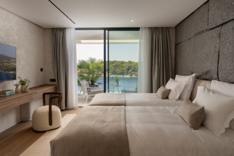 Schlafzimmer mit Betten an einer natürlichen Steinmauer und einer Terrasse mit Meerblick in der Villa Klara