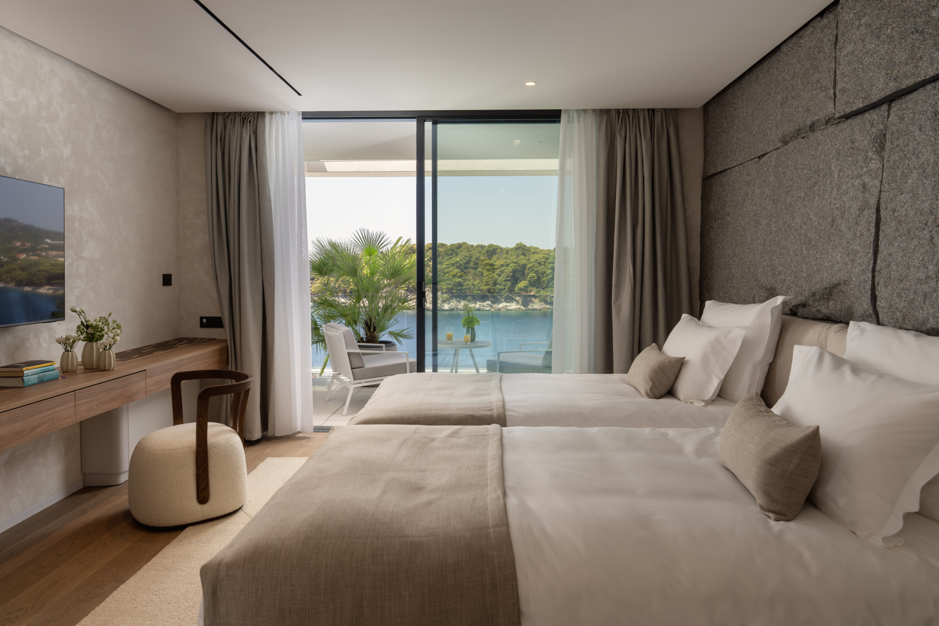 Schlafzimmer mit Betten an einer natürlichen Steinmauer und einer Terrasse mit Meerblick in der Villa Klara