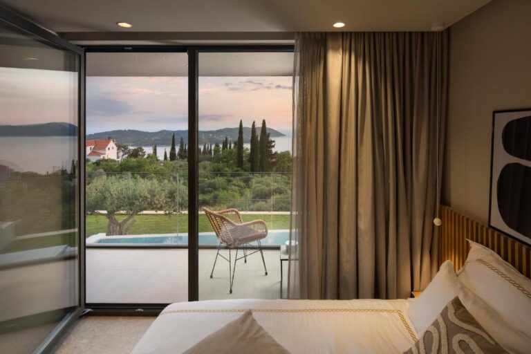 Schlafzimmer mit Kingsize-Bett, das auf eine Terrasse mit Pool, Olivenbäumen und Meerblick führt, in der Villa Ó